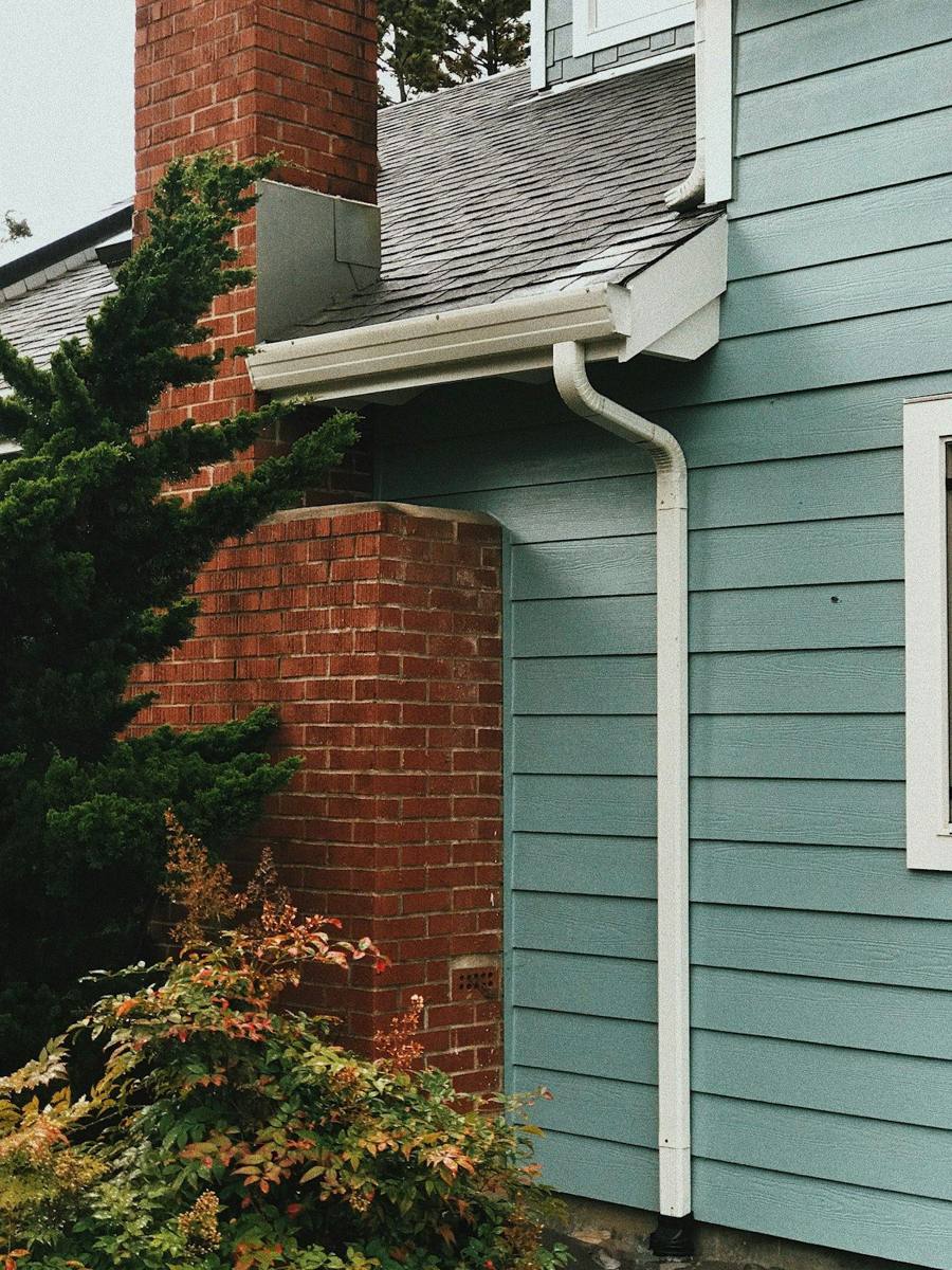 White downspout running down blue siding beside a brick chimney